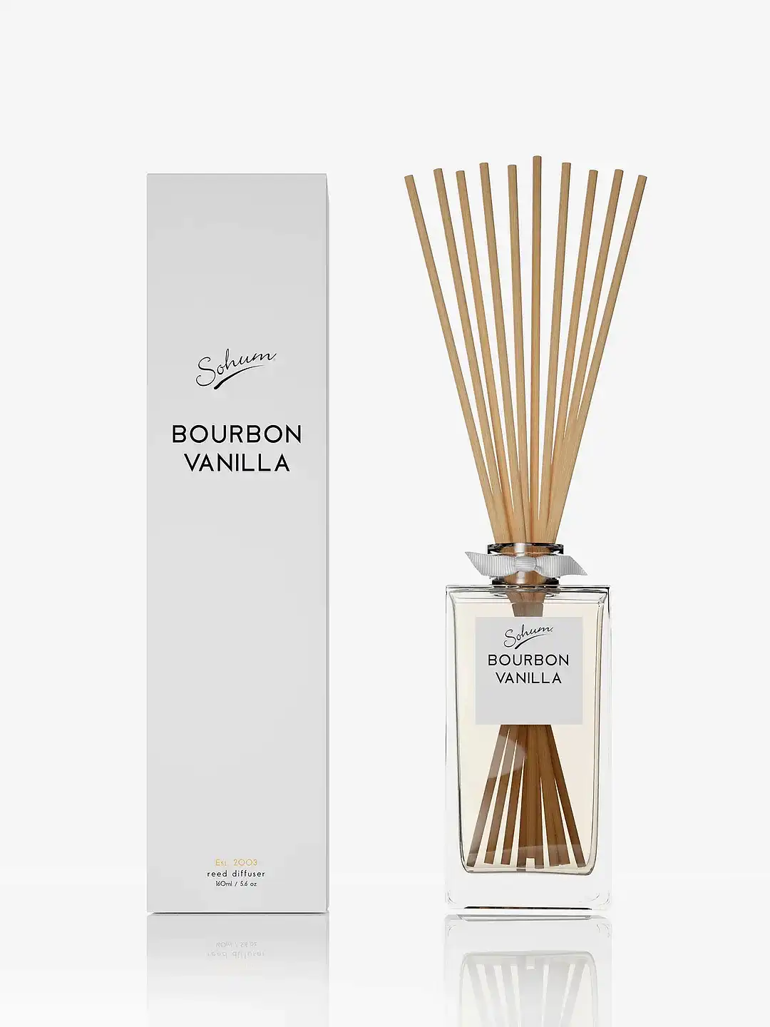 A glass bottle of "Sohum Fragrance Diffuser" by Flowers on Norton St is displayed alongside its matching rectangular box, showcasing several long, slender natural fiber reeds. The bottle contains a clear liquid infused with a refined fragrance. Both items are elegantly set against a plain white background.