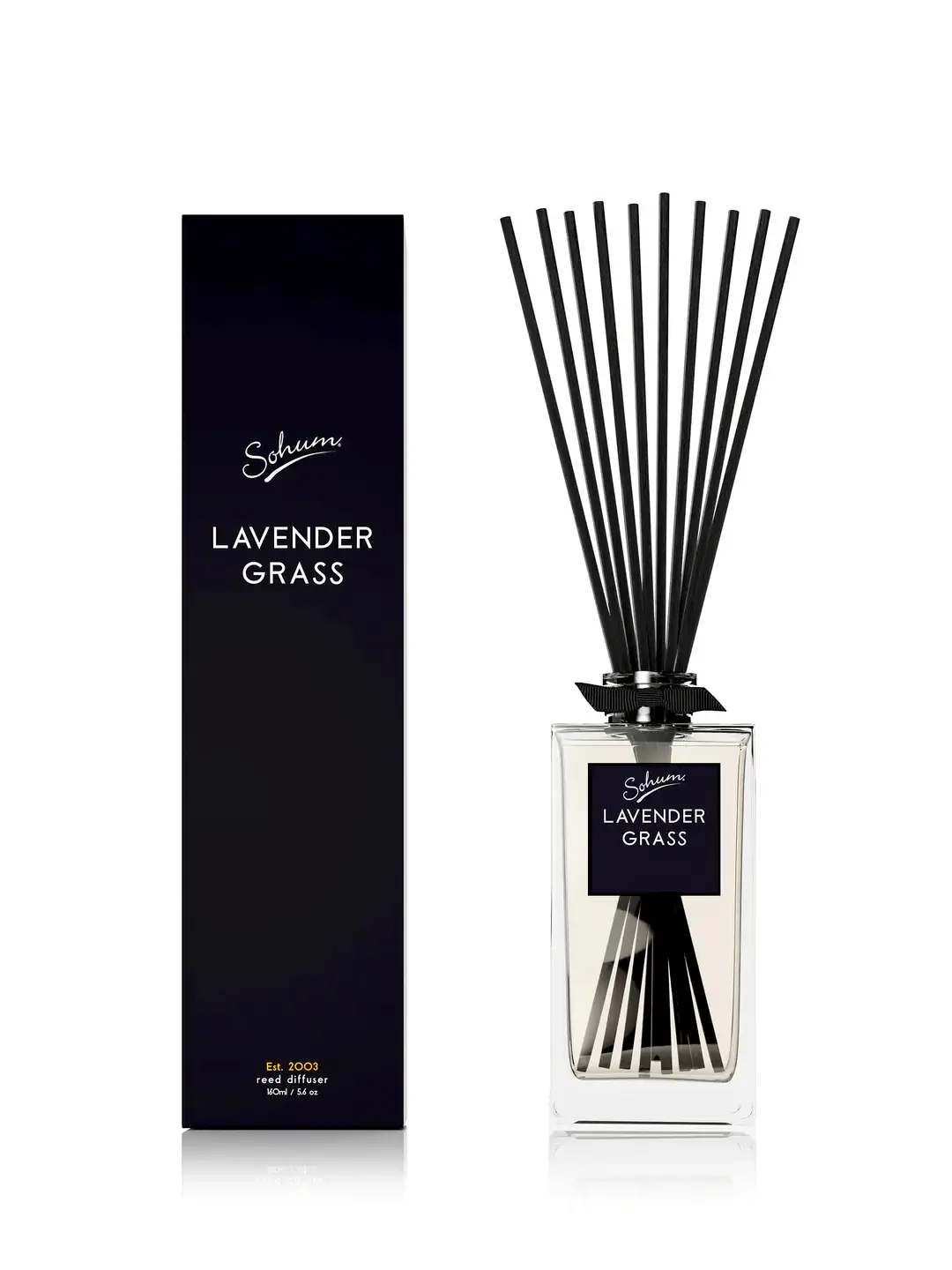 A clear glass reed diffuser from the Flowers on Norton St brand, labeled "Sohum Fragrance Diffuser," with black natural fiber reeds delivers a lovely scent, elegantly positioned next to its matching black box packaging.