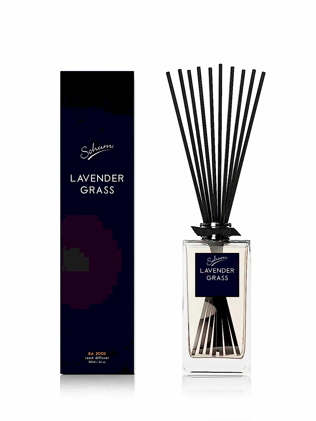 The Sohum Fragrance Diffuser by Flowers on Norton St, featuring natural fiber reeds in "Lavender Grass," stands elegantly next to its matching black box packaging on a white background.