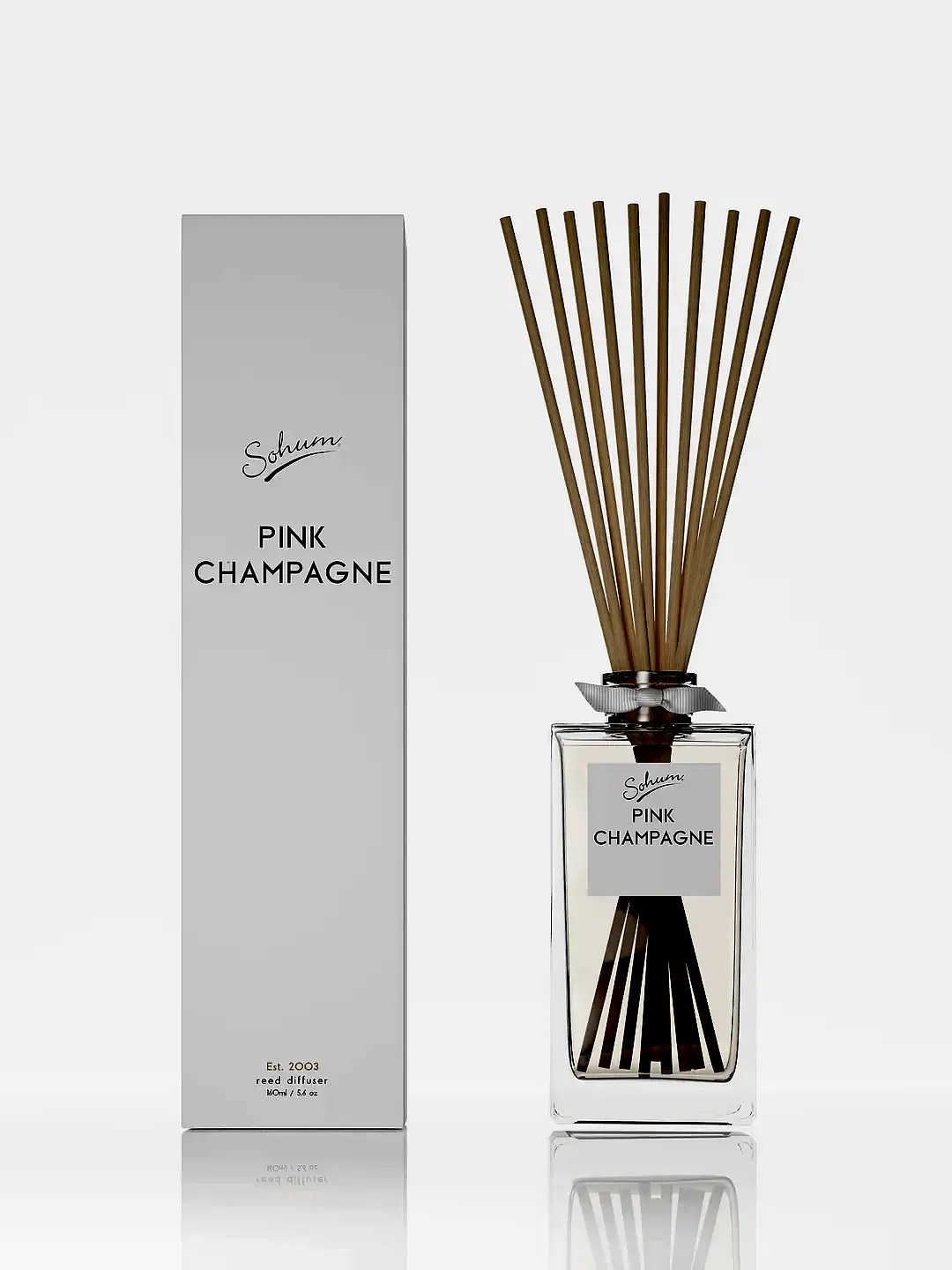 The "Sohum Fragrance Diffuser" by Flowers on Norton St features a scent labeled "Pink Champagne" with natural fiber reeds in a glass bottle. The minimalistic packaging includes a white box on the left displaying the same fine fragrance branding of "Schuum Pink Champagne.