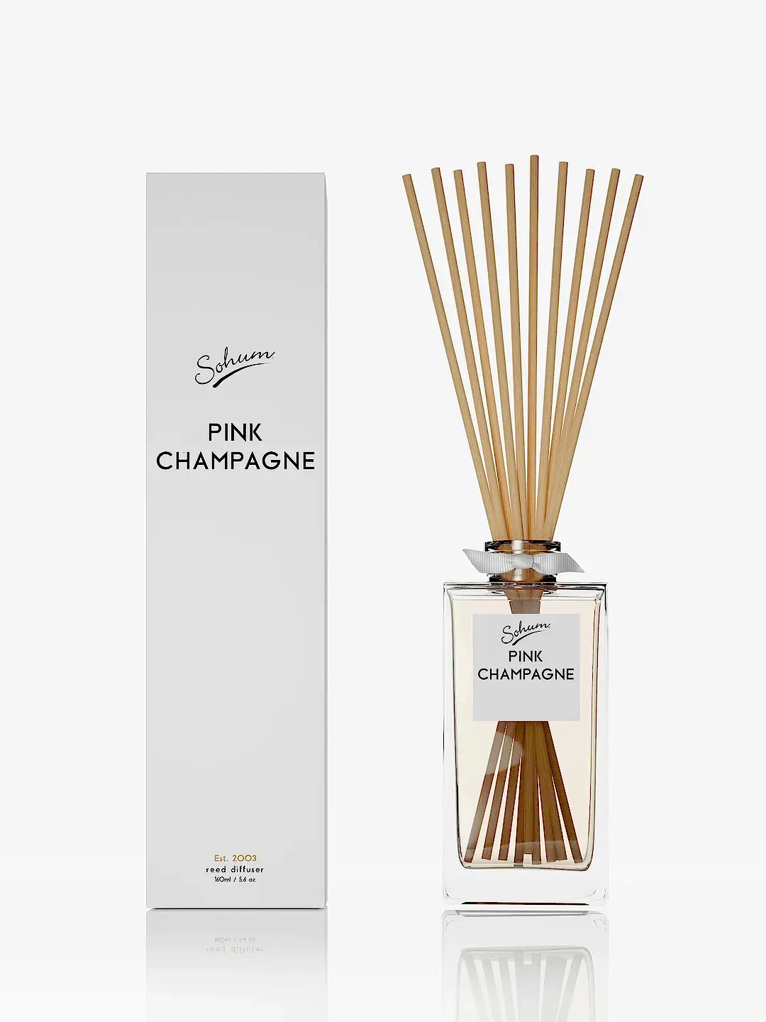 A Sohum Fragrance Diffuser named "Pink Champagne," featuring natural fibre reeds, is elegantly displayed next to its matching white box packaging, both bearing the name "Pink Champagne." Both the diffuser and box prominently showcase the brand name "Flowers on Norton St," representing the pinnacle of fine fragrance.