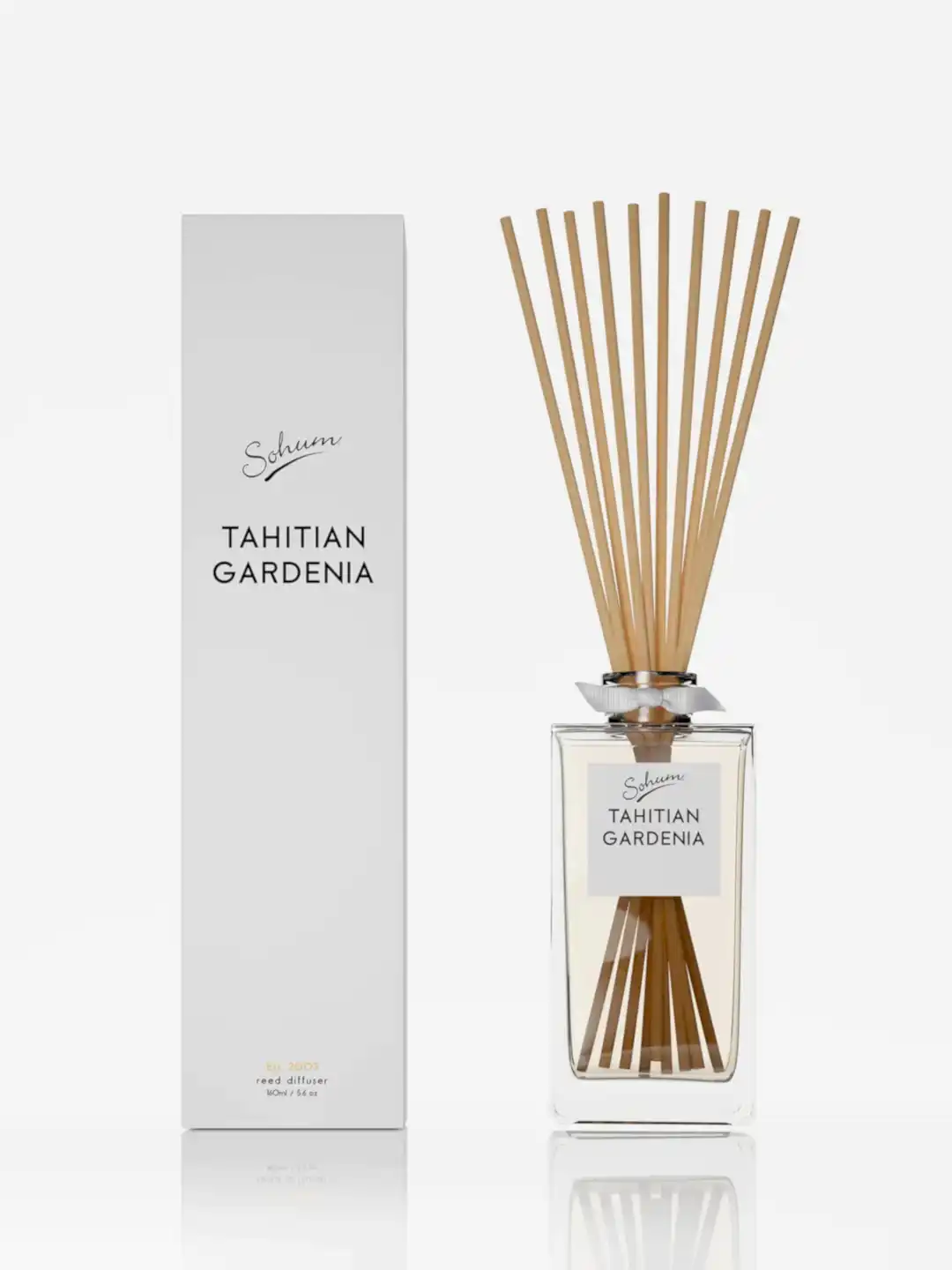 A bottle of the Sohum Fragrance Diffuser by Flowers on Norton St sits elegantly next to its matching white box. Filled with a fine fragrance and topped with natural fiber reeds, it's designed to elevate home ambiance through exquisite fragrance diffusion.