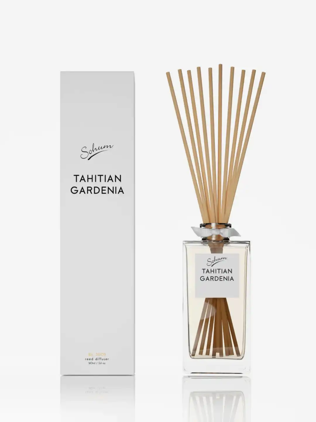 A bottle of the Sohum Fragrance Diffuser by Flowers on Norton St sits elegantly next to its matching white box. Filled with a fine fragrance and topped with natural fiber reeds, it's designed to elevate home ambiance through exquisite fragrance diffusion.