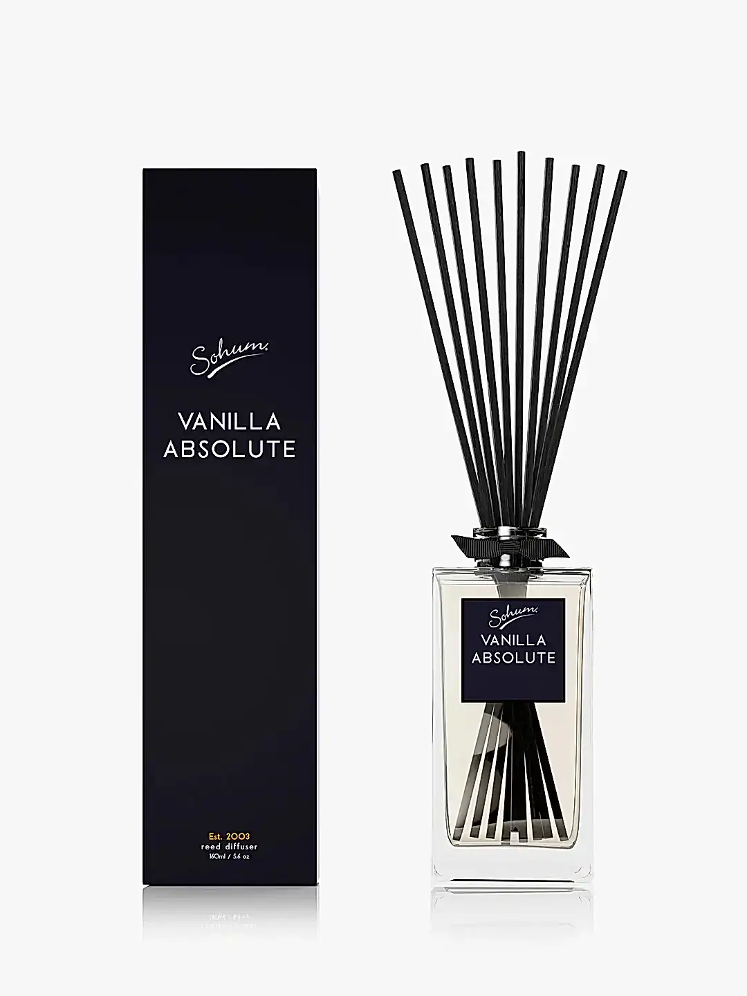A black, rectangular box labeled "Flowers on Norton St Sohum Fragrance Diffuser" stands beside a clear glass reed diffuser bottle. Designed for fine fragrance lovers, the bottle features natural fiber reeds extending from it, enhancing the pleasing aroma with its light-colored liquid.