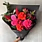 A bouquet featuring FlowersonNortonSt's Florist Choice - Red Nina Bouquet with vibrant Red Nina and pink roses, pink dahlias, and seasonal blooms with green leaves, elegantly wrapped in black paper against a gray background.