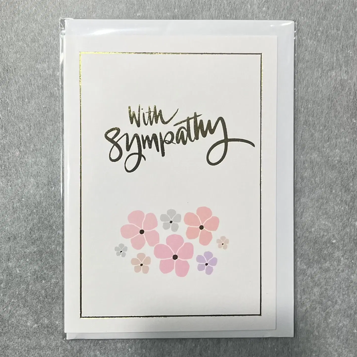 A special Sympathy Card from Flowers on Norton St displays "With Sympathy" in elegant script at the top, accompanied by pastel flowers in shades of pink, purple, and gray that capture a florist's delicate touch. The card is embellished with a thin gold border and set against a gray background.