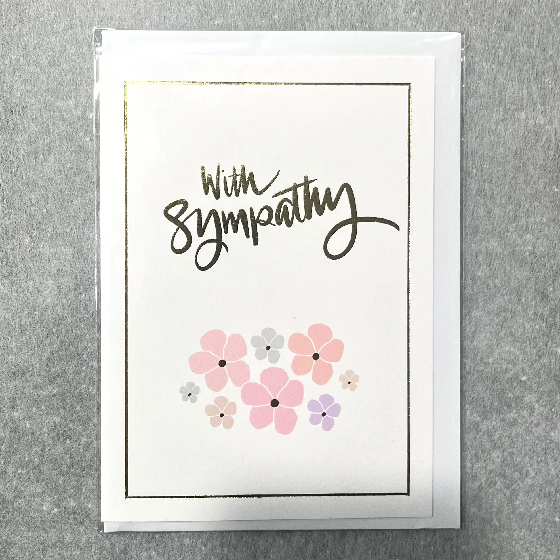 A special Sympathy Card from Flowers on Norton St displays "With Sympathy" in elegant script at the top, accompanied by pastel flowers in shades of pink, purple, and gray that capture a florist's delicate touch. The card is embellished with a thin gold border and set against a gray background.