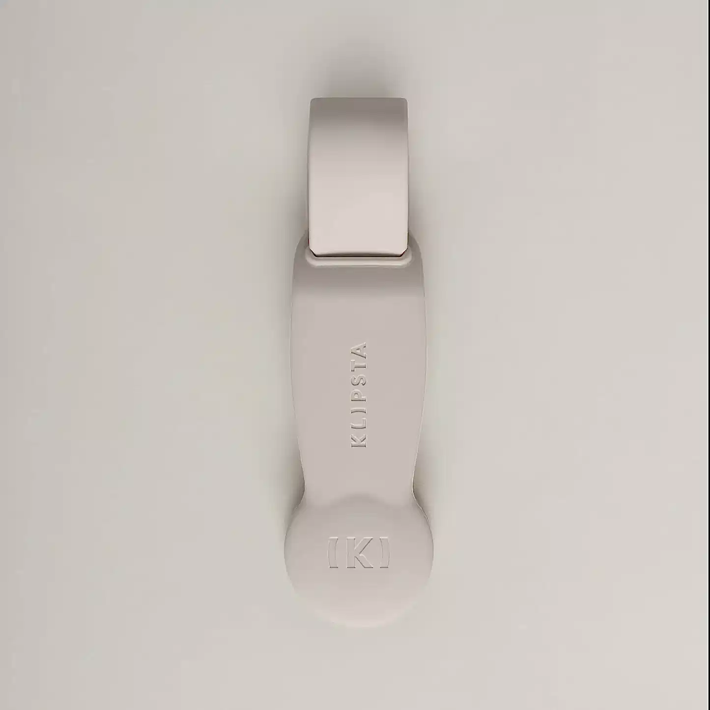 A beige, minimalist accessory from Flowers on Norton St's Accessories by Klipsta collection highlights the brand’s distinctive style with a rounded end and a circular emblem featuring "K" in brackets. These multifunctional accessories easily enhance your look, set elegantly against a light gray background.