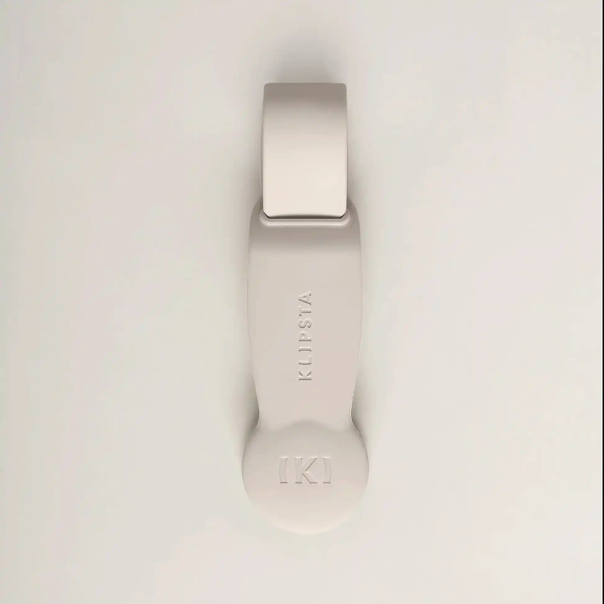 A beige, minimalist accessory from Flowers on Norton St's Accessories by Klipsta collection highlights the brand’s distinctive style with a rounded end and a circular emblem featuring "K" in brackets. These multifunctional accessories easily enhance your look, set elegantly against a light gray background.