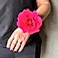 Dressed in a sleek black ensemble, an individual elegantly displays the Flowers on Norton St's "Modern Wrist Corsage," highlighted by a vibrant pink rose. The subtle gleam of their purple-painted nails and ring against a gray backdrop adds an air of sophistication, perfect for school formals or any elegant occasion.