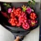 The Florist Choice - Red Nina Bouquet by FlowersonNortonSt boasts vibrant Red Nina and Colombian roses with purple dahlias and green leaves, beautifully wrapped in black paper.