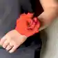A person wearing the Modern Wrist Corsage by Flowers on Norton St, featuring a large red rose, complements their black shirt. Their hand, adorned with rings, rests casually as they prepare for the formal event.