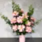 The Ruby Rose Valentine's Vase from Flowers on Norton St showcases Colombian roses with lush green foliage, set against a light gray textured background for an elegant and romantic touch to any setting.