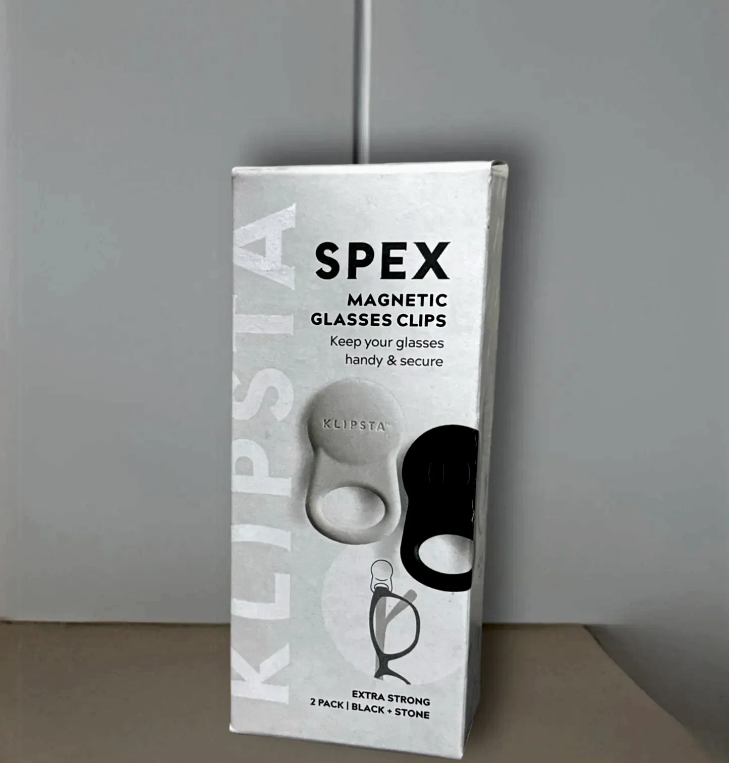 The image showcases an "Accessories by Klipsta" package, under the Flowers on Norton St brand, which includes versatile glasses clips. The text reads "Keep your glasses handy & secure," featuring both a white and black clip. A small diagram demonstrates how the clip securely holds glasses, highlighting "Accessories by Klipsta" as essential for eyewear organization.