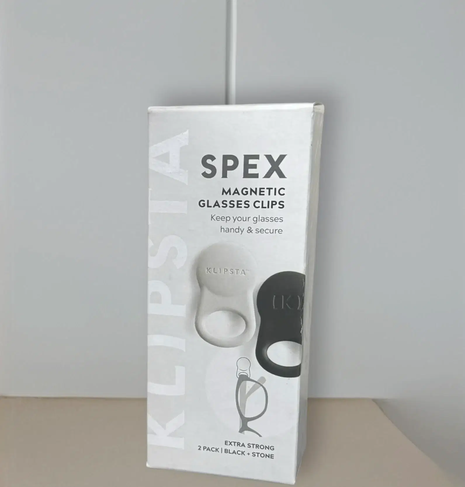The image showcases an "Accessories by Klipsta" package, under the Flowers on Norton St brand, which includes versatile glasses clips. The text reads "Keep your glasses handy & secure," featuring both a white and black clip. A small diagram demonstrates how the clip securely holds glasses, highlighting "Accessories by Klipsta" as essential for eyewear organization.