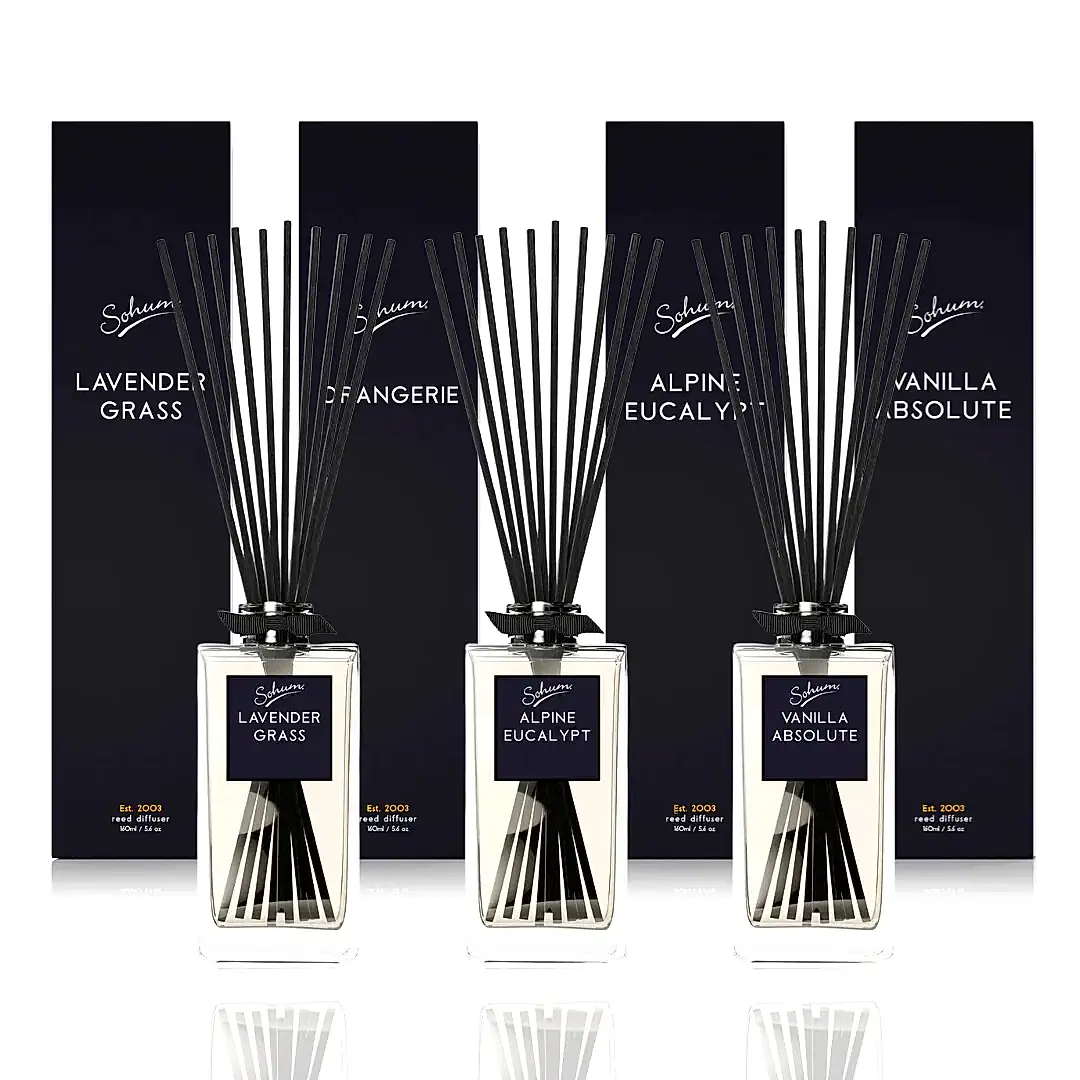 Three Sohum Fragrance Diffusers by Flowers on Norton St, featuring tall black sticks and matching containers, are displayed in front of dark boxes. The exquisite scents offered are Lavender Grass, Alpine Eucalypt, and Vanilla Absolute.