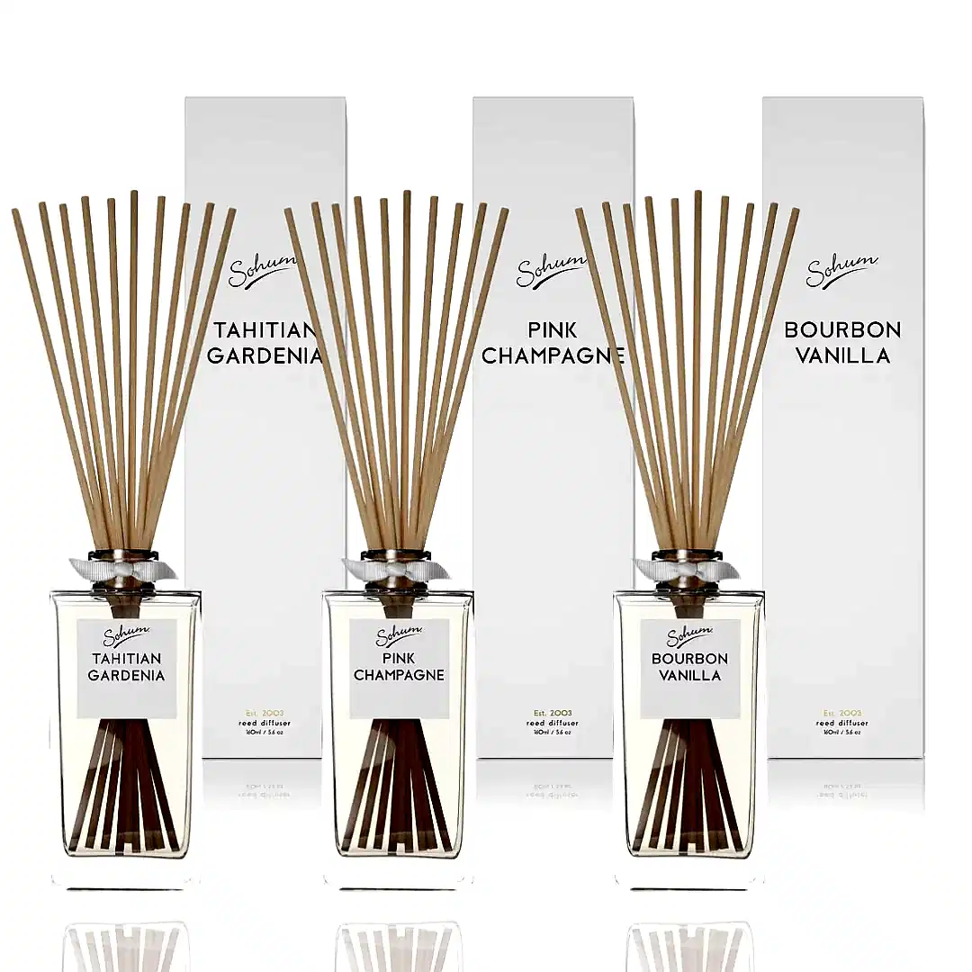 Three fragrance diffuser bottles featuring natural fiber reeds are elegantly arranged in front of their boxes. The scents—Tahitian Gardenia, Pink Champagne, and Bourbon Vanilla—are housed in clear bottles with a minimalist design, each label prominently displaying the brand name "Flowers on Norton St," exemplifying fine fragrance at its best.