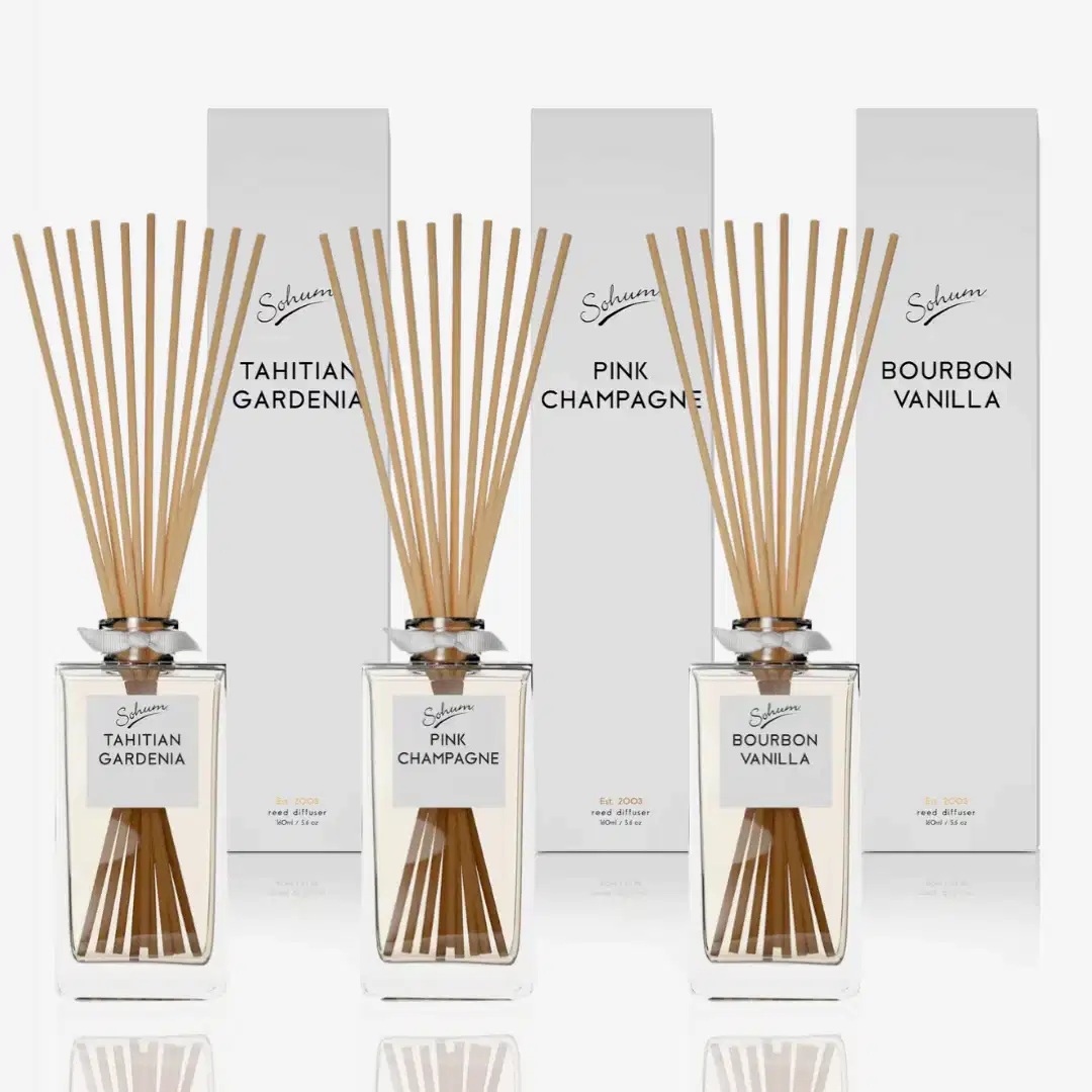 Three fragrance diffuser bottles featuring natural fiber reeds are elegantly arranged in front of their boxes. The scents—Tahitian Gardenia, Pink Champagne, and Bourbon Vanilla—are housed in clear bottles with a minimalist design, each label prominently displaying the brand name "Flowers on Norton St," exemplifying fine fragrance at its best.