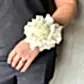 A person displays elegance with the Modern Wrist Corsage by Flowers on Norton St, featuring a striking large white flower on their wrist. Complementing the corsage is a ring adorning their finger, paired seamlessly with sleek black attire. Set against a neutral background, this image beautifully captures an outfit ideal for school formals or any formal occasion.