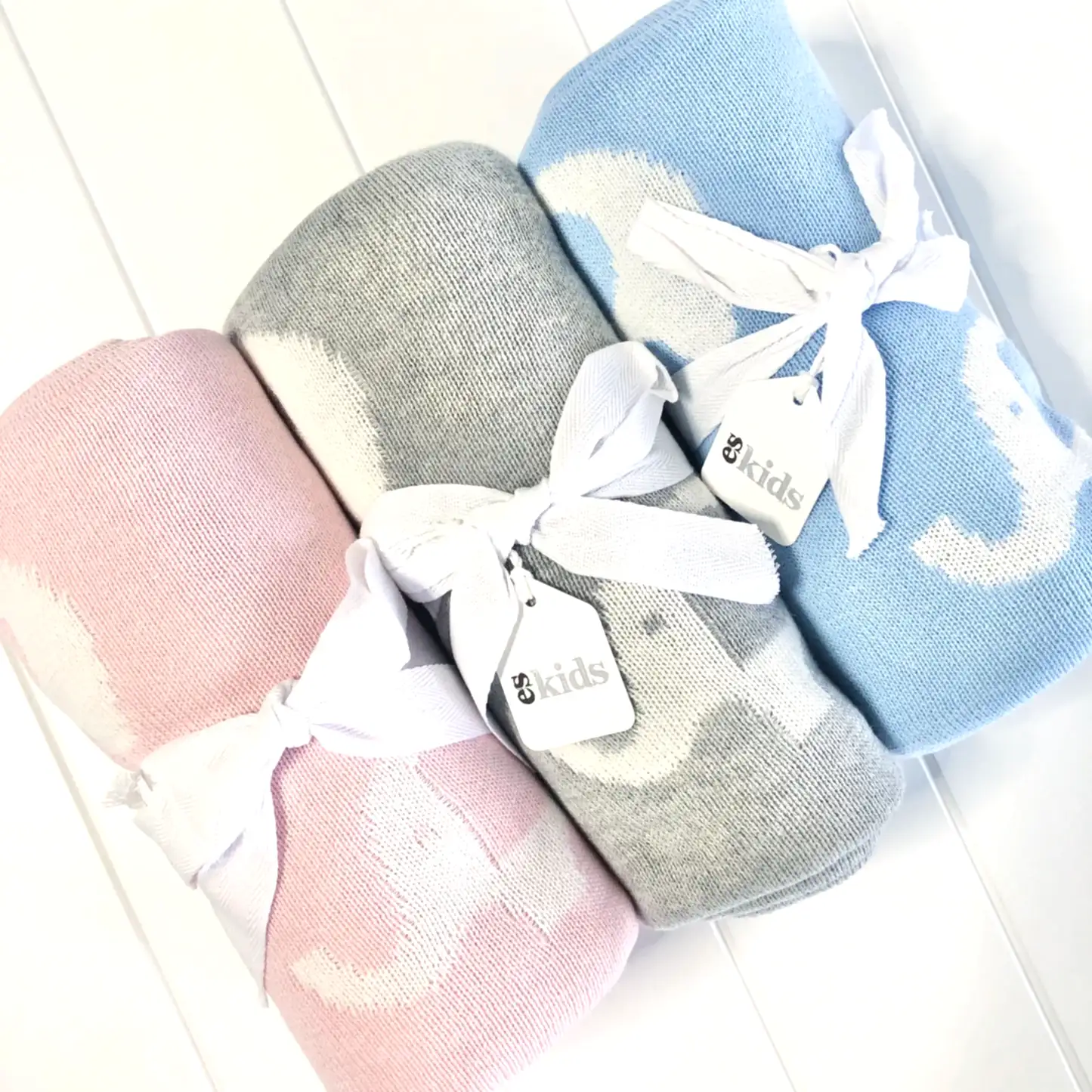 The set includes three Ellie Baby Blankets from FlowersonNortonSt in pink, gray, and blue, each adorned with a white ribbon and a small "kids" label tag. Crafted for supreme softness, these blankets are elegantly displayed against a white background.