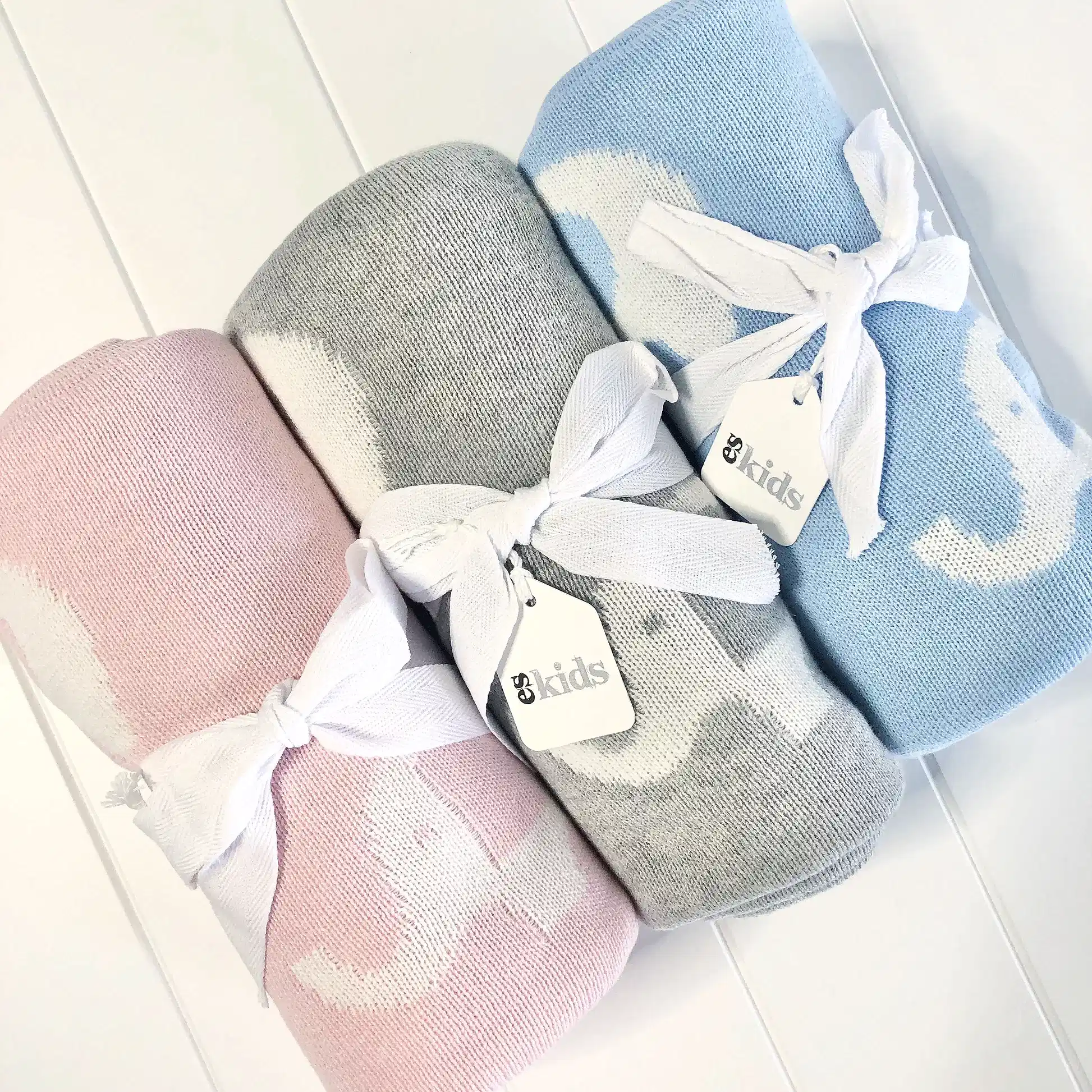 The set includes three Ellie Baby Blankets from FlowersonNortonSt in pink, gray, and blue, each adorned with a white ribbon and a small "kids" label tag. Crafted for supreme softness, these blankets are elegantly displayed against a white background.
