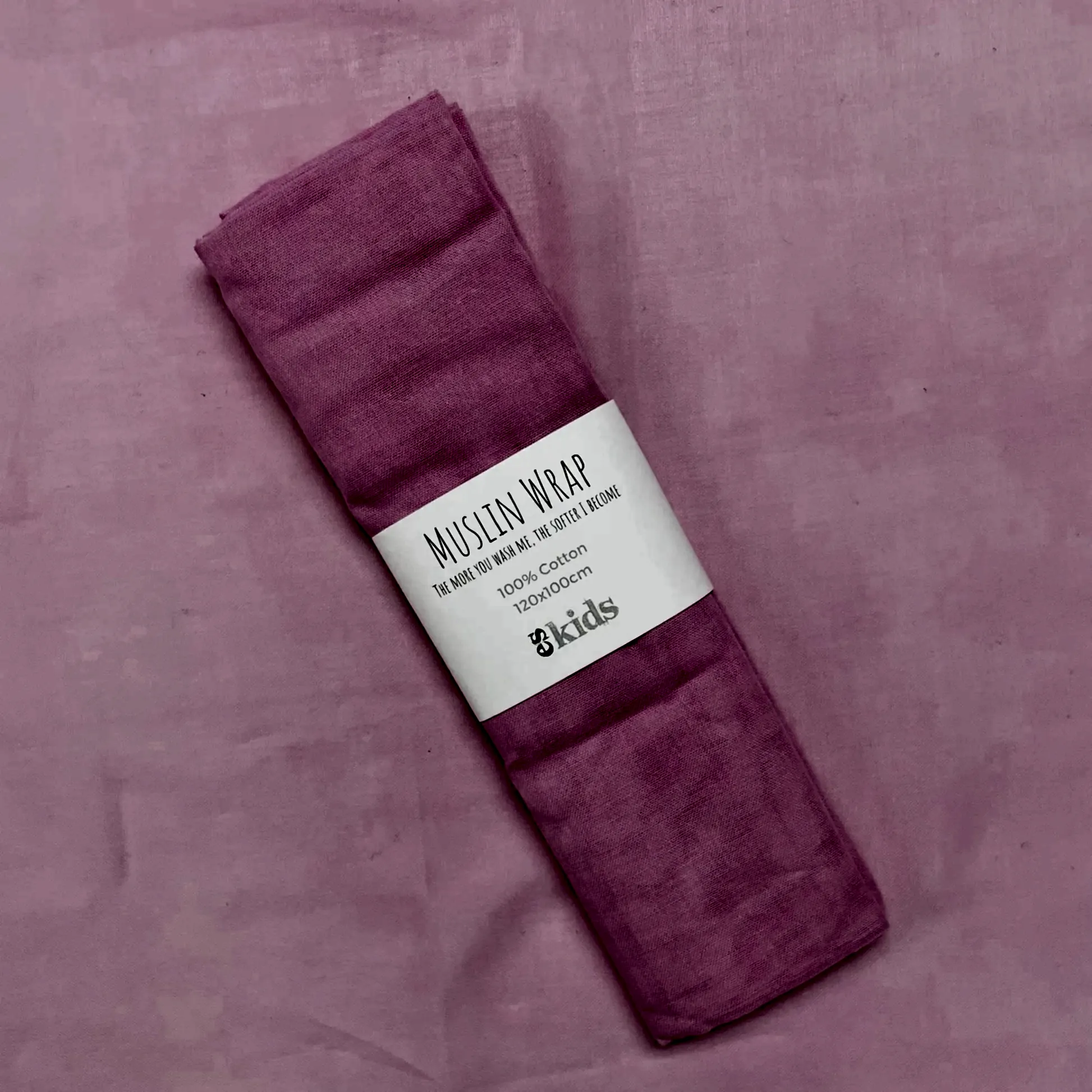 A FlowersonNortonSt Muslin Wrap, designed for wrapping babies, comes in a neatly folded pink muslin fabric secured with a white label featuring text. The pink background offers a cohesive color scheme, making this Muslin Wrap appear lightweight and gentle, perfect for kids.