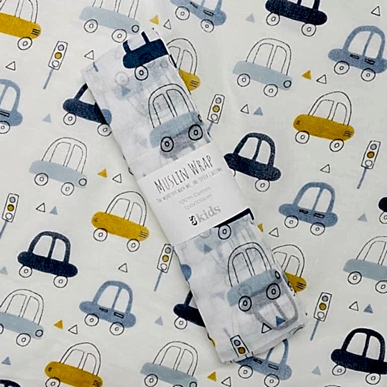 A delicate muslin wrap featuring a pastel print of blue, gray, and yellow cars, traffic lights, and triangles is ideal for swaddling babies. It is elegantly displayed on a coordinating background, complete with a label stating "Muslin Wraps by FlowersonNortonSt, 100% Cotton.