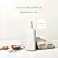 A bottle of AL.IVE BODY | Home & Kitchen natural hand wash, by Flowers on Norton St, adorned with Watermelon & Lime scents, is elegantly displayed on stone alongside a small wooden spoon and a bowl of pink Himalayan salt. As essential kitchen companions, these vibrant fragrances infuse your home with refreshing aromas. Text reads "In Store Now.