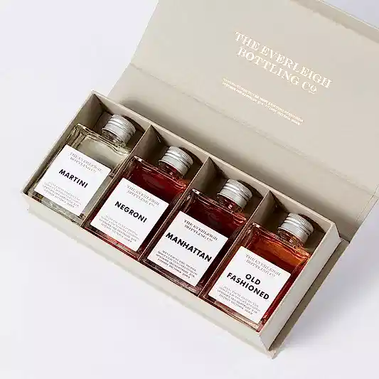 A beige box reveals the Famous Four—a curated set of square bottles highlighting timeless cocktails: Martini, Negroni, Manhattan, and Old Fashioned. Each bottle is discreetly marked with "The Everleigh Bottling Co." by FlowersonNortonSt.