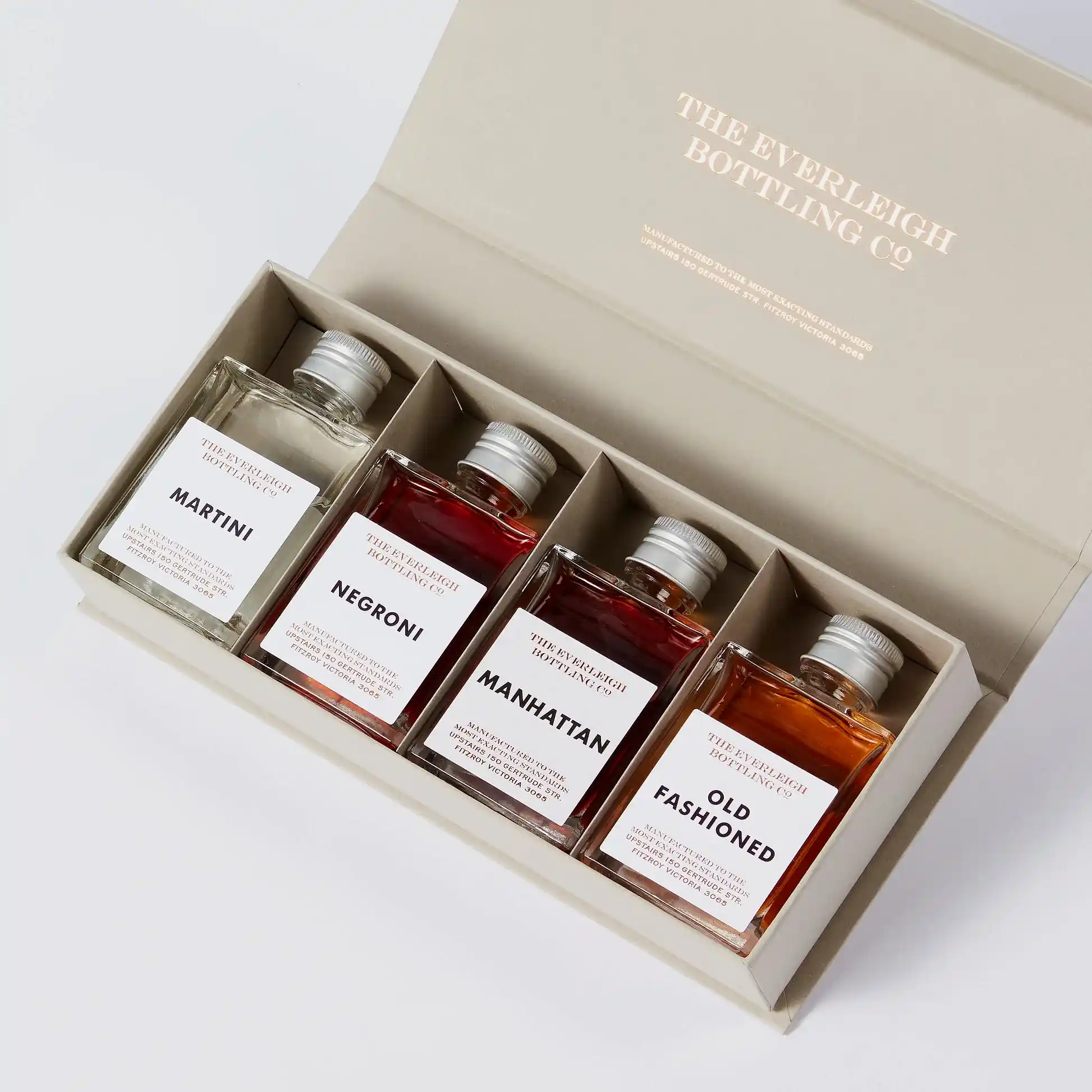 A beige box reveals the Famous Four—a curated set of square bottles highlighting timeless cocktails: Martini, Negroni, Manhattan, and Old Fashioned. Each bottle is discreetly marked with "The Everleigh Bottling Co." by FlowersonNortonSt.