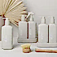 A selection of beige pump bottles labeled "AL.IVE BODY | Home & Kitchen" by Flowers on Norton St showcases hand wash and skincare products infused with the invigorating scents of Lemon & Pomegranate. These elegantly arranged bottles sit on a white surface, enhanced by a wooden dish brush and beige leaf decorations, bringing stylish kitchen essentials to your home.