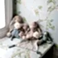 A selection of plush teddy bears, featuring a delightful Barney Bear, along with other stuffed animals, is displayed on a cushioned bench by the window. The wallpaper showcases an intricate floral pattern adorned with green vines and white flowers from Flowers on Norton St, cultivating a soft and welcoming ambiance.