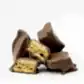 A stack of Whisk & Pin Honey Crunch Rocks by FlowersonNortonSt sits against a white background. One piece is cut open, showcasing the airy honeycomb center encased in smooth Belgian chocolate, made with rich Blue Mountains honey.