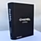 A black hardcover "Chanel Catwalk | Gift Book" by FlowersonNortonSt lies on a white surface against a light gray background, showcasing Chanel collections. The spine proudly features "CHANEL CATWALK." Published by Thames & Hudson.