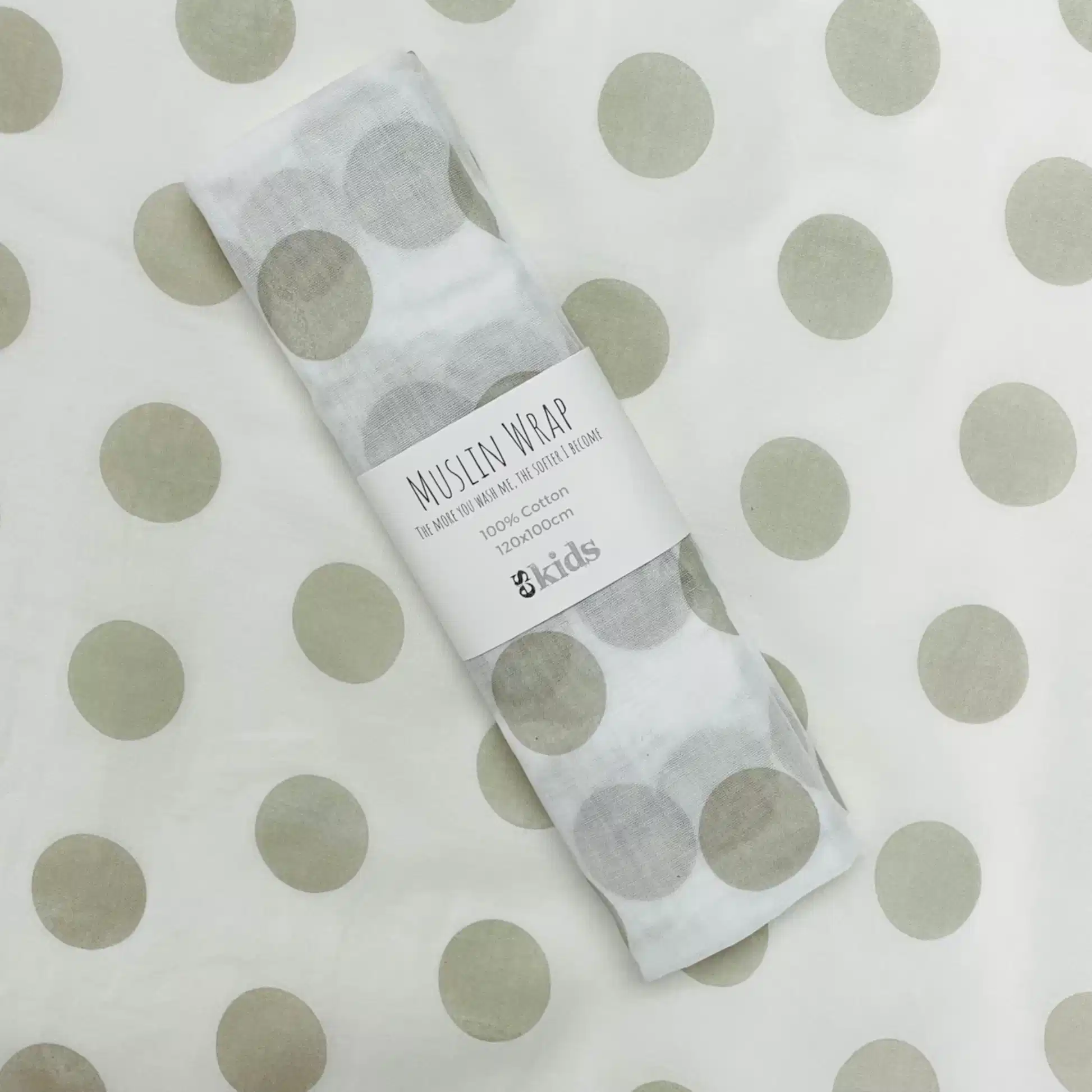 A folded Muslin Wraps by FlowersonNortonSt, featuring large grey polka dots, sits against a matching polka dot background—ideal for wrapping babies. The soft muslin, made from 100% cotton, is accentuated with a white label displaying the brand's text and logo.