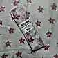 A Muslin Wrap from FlowersonNortonSt, featuring a charming pink star pattern, rests on matching fabric. The label indicates it's made of 100% cotton, ideal for swaddling and providing soft comfort.