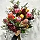 Introducing the "Australiana" by FlowersonNortonSt—a stunning bouquet showcasing an array of Australian wildflowers. This vibrant arrangement features pink proteas, orange and yellow banksias, and red leucadendrons, beautifully intertwined with orchids and eucalyptus, all complemented by lush greenery set against a light background.