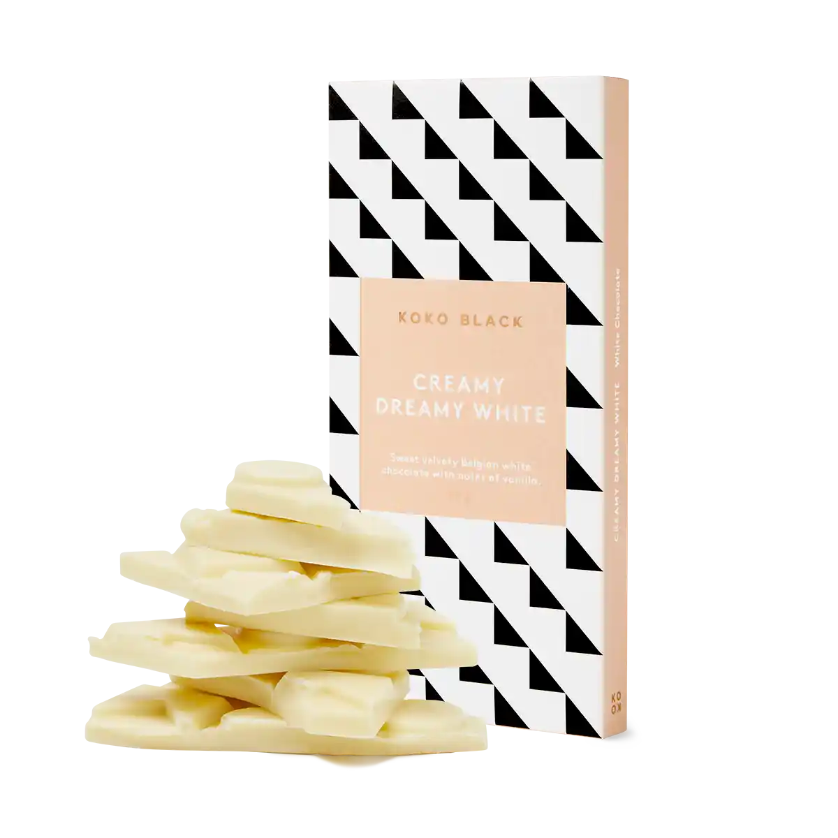 A stack of white chocolate pieces invites indulgence in front of a FlowersonNortonSt Koko Black Chocolate Block. The packaging, featuring a black and white geometric pattern with peach-colored accents, emphasizes its sustainably sourced cocoa and natural ingredients.