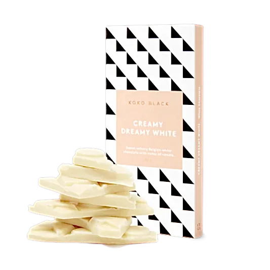 A stack of creamy white chocolate pieces stands before geometric-patterned packaging labeled "Koko Black White Chocolate" by Flowers on Norton St. The peach-and-white packaging with black triangles hints at rich vanilla notes within.