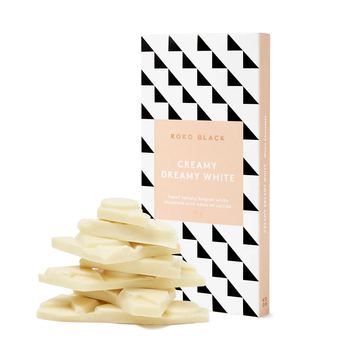 A stack of creamy white chocolate pieces stands before geometric-patterned packaging labeled "Koko Black White Chocolate" by Flowers on Norton St. The peach-and-white packaging with black triangles hints at rich vanilla notes within.