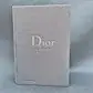 The Dior Catwalk Gift Book, a plain gray hardcover from FlowersonNortonSt, elegantly showcases Dior's haute couture with minimalist typography reflecting Maria Grazia Chiuri's vision. The publisher "Thames & Hudson" is placed on the bottom left against a textured light background.