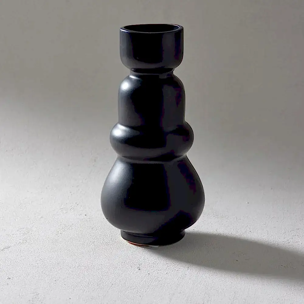 A sleek, black handcrafted ceramic vase from Flowers on Norton St, featuring a unique sculptural design with rounded tiers reminiscent of the Klein Vase, set against a neutral gray background.