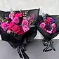 Two vibrant Hot Pink Pop Mixed Flower Bouquets from Flowers on Norton St are wrapped in black paper, showcasing an enchanting mix of hot pink pop roses, purple dahlias, and dark foliage. Each bouquet is elegantly tied with a black ribbon labeled "FLOWERS FOR NOW," beautifully contrasting against a light gray background.