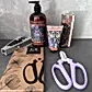 The Budding Florist Kit from Flowers on Norton St includes a lavender and rosemary hand care set featuring a hand wash, hand cream, and a decorative box. Next to them are purple-handled floral secateurs packaged in a brown "Flower Snips" box. On the left, there is also a gray box that completes this charming kit.