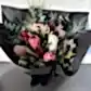 Introducing the "Little Native Bunch" by Flowers on Norton St: A striking bouquet showcasing native flora and a diverse array of protea flowers, complemented with lush greenery and subtle pink accents. This exquisite arrangement is beautifully wrapped in elegant black paper and tied with a chic black ribbon, all set against a light gray backdrop.