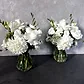 Featuring the Lovely Vintage Vases by FlowersonNortonSt, this table centerpiece showcases elegant white floral arrangements with roses, dahlias, and greenery. Set against a textured gray background, it creates a simple and classy display with seasonal blooms.
