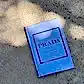 A book titled "Little Book of Style" by Flowers on Norton St rests on a textured concrete surface, partially in shadow. A must-have for any fashion lover, this edition features a light purple cover with a minimalist design. Shadows of nearby leaves are visible on the ground.