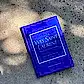 A book with a blue cover titled "Little Book of Style" by Flowers on Norton St, ideal for anyone passionate about fashion, is placed on a textured stone surface where gentle shadows gracefully drape over it. As part of the "Little Guides to Style," it honors legendary fashion houses.