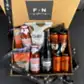 The "Celebration in a Box" by Flowers on Norton St includes two jars of Don Antonio's Sugo di Pomodoro alla Calabrese, a bag of Quillo potato chips, a bottle of wine, two packs of Griffin's cookies, and four cans of beer. Elegantly tied with black ribbons printed with "F+N gifting," it is available for same-day delivery in Sydney.