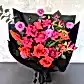 The Florist Choice - Red Nina Bouquet by FlowersonNortonSt features vibrant Red Nina and Colombian roses, bright pink blooms, and lush green foliage, elegantly wrapped in black paper with a black ribbon, set on a light gray backdrop.